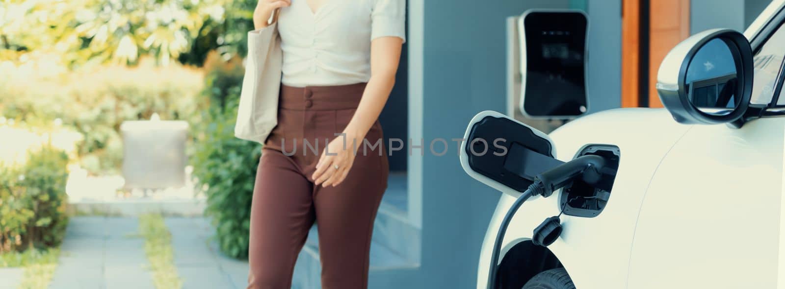 Progressive asian woman and electric car with home charging station. Concept of the use of electric vehicles in a progressive lifestyle contributes to a clean and healthy environment.