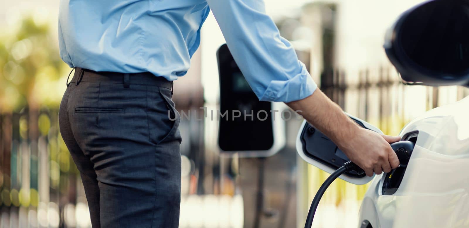 Closeup progressive man holding EV charger plug from public charging station for electric vehicle with background of residential building as concept eco-friendly sustainability energy car concept.