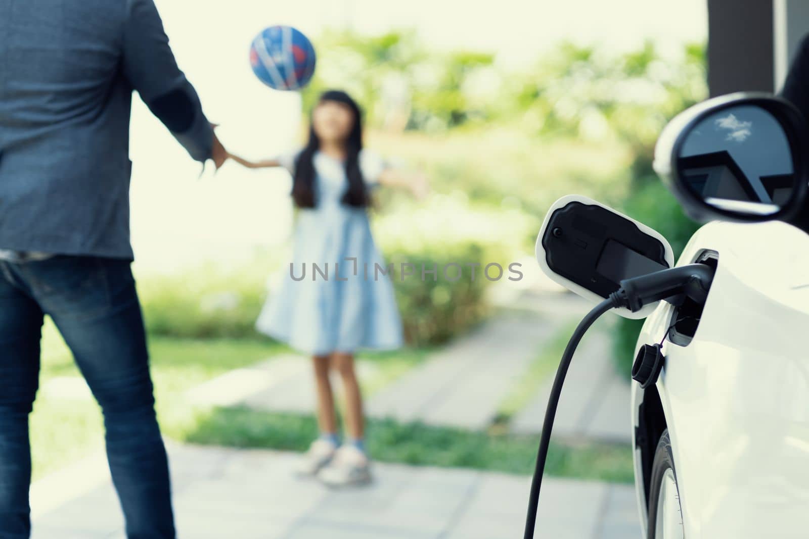 Progressive dad and daughter charging EV car from home charging station. by biancoblue