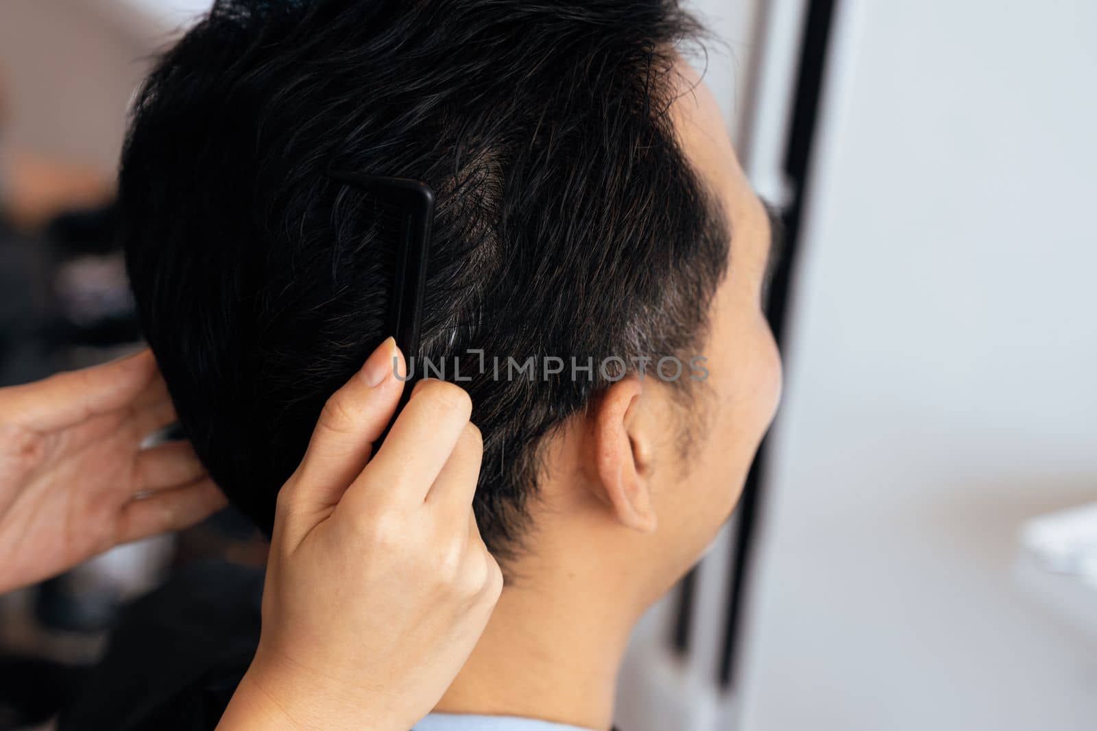 Closeup asian female barber making haircut for male customer with male hairstyle in qualified barbershop. Men's hairstyling by a scissor and comb in hair salon concept.