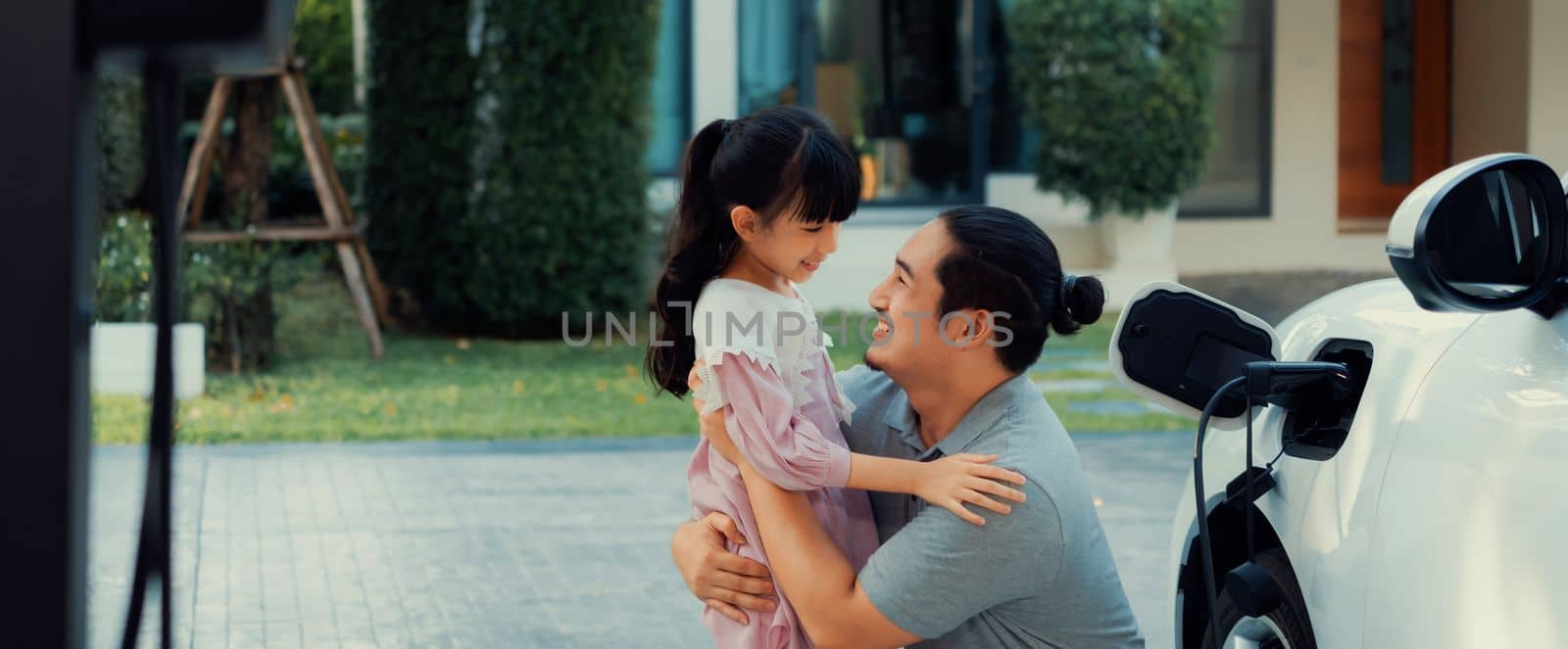 Progressive concept of father and daughter with EV car and home charging station by biancoblue