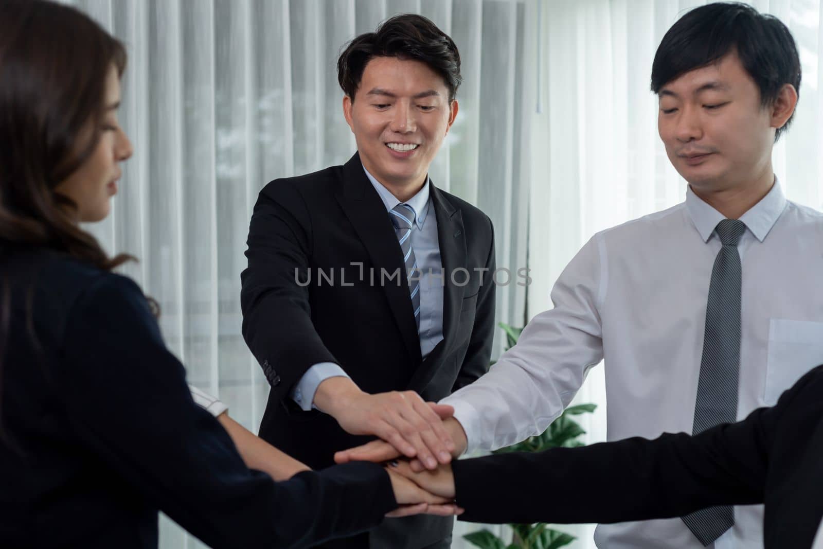 Closeup business team of suit-clad businessmen and women join hand stack together and form circle. Colleague collaborate and work together to promote harmony and teamwork concept in office workplace.