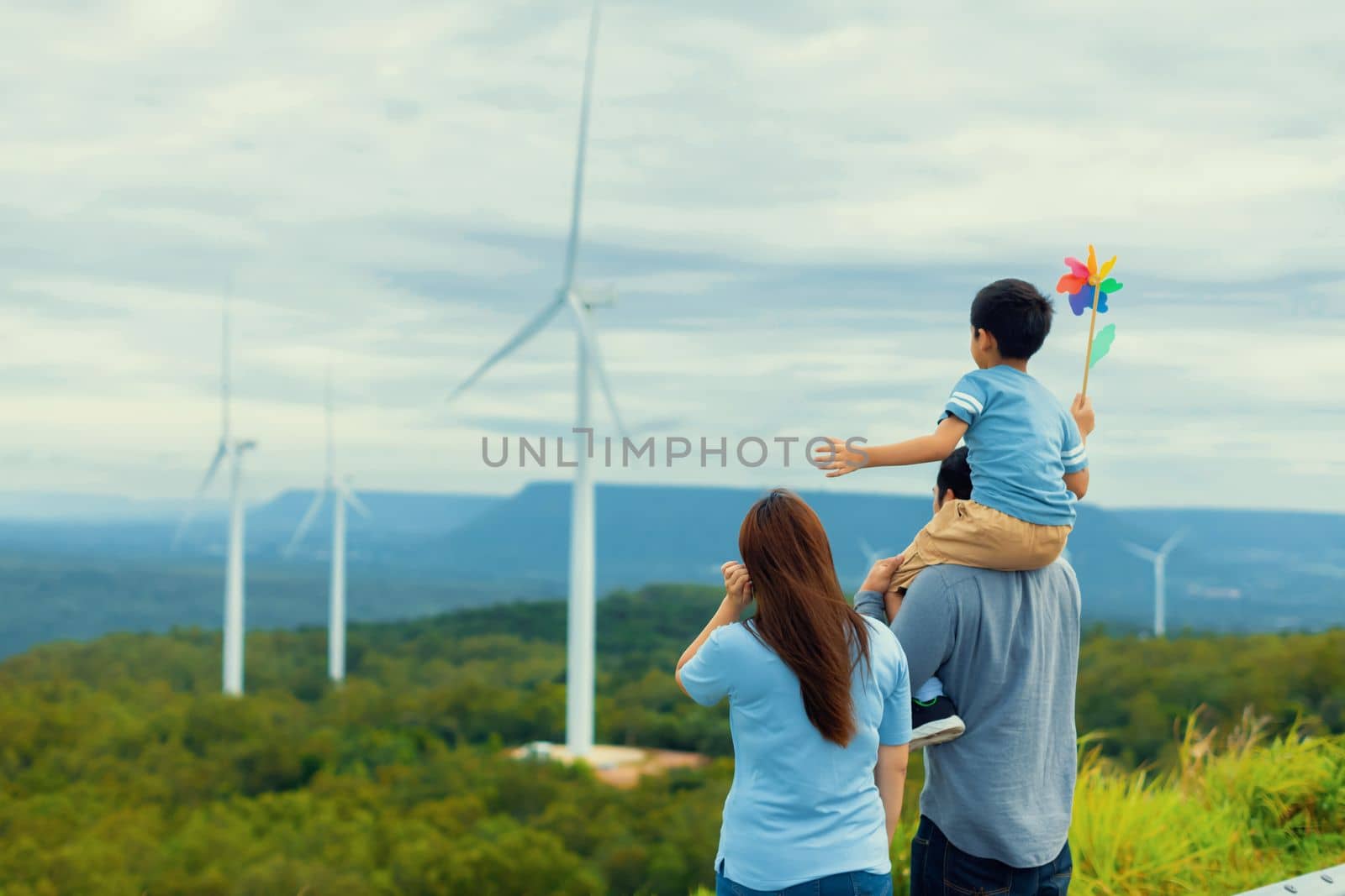 Progressive happy family enjoying their time at wind farm for green energy production concept. Wind turbine generators provide clean renewable energy for eco-friendly purposes.
