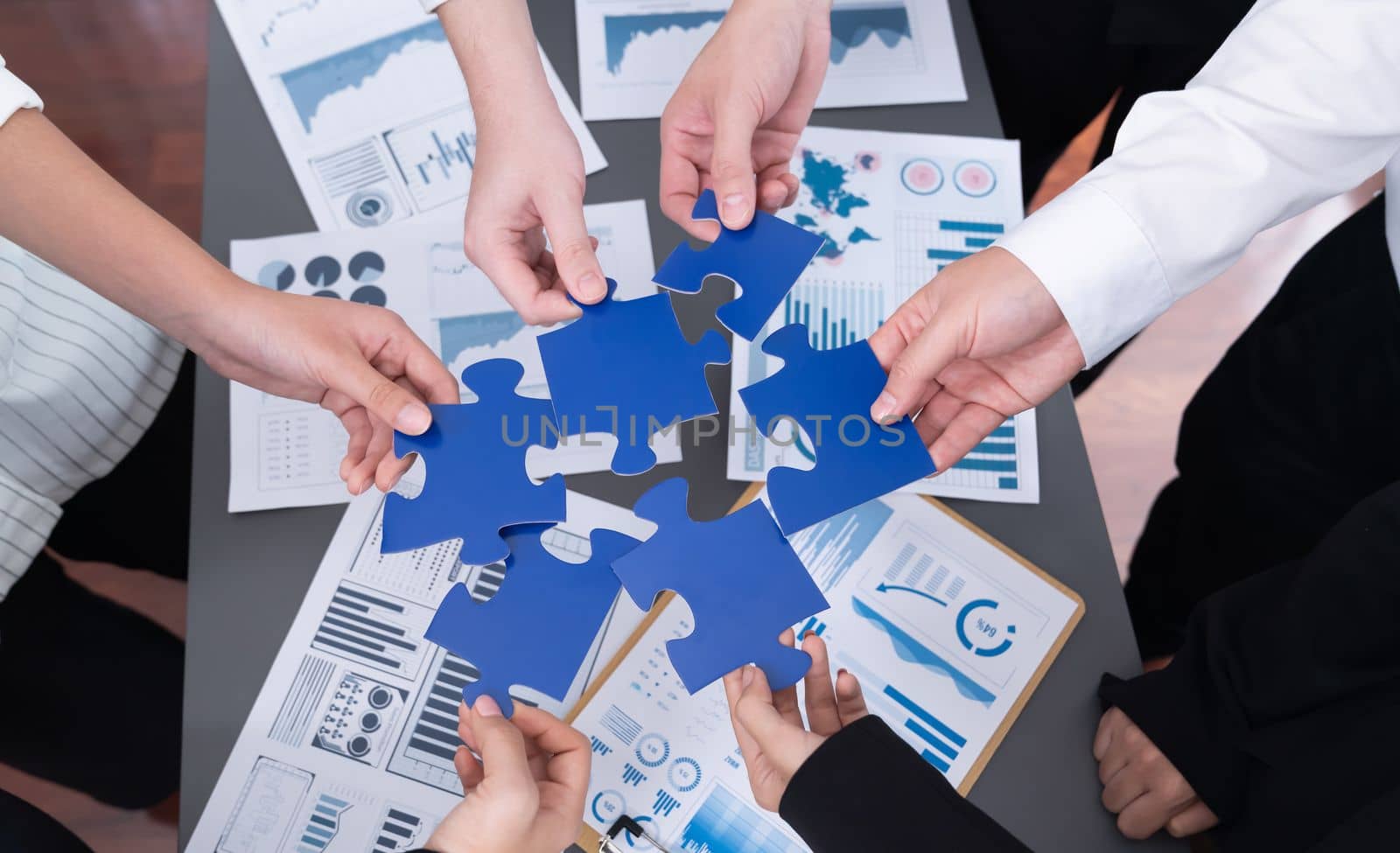 Closeup top view business team of office worker putting jigsaw puzzle together over table filled with financial report paper in workplace with manager to promote harmony concept in meeting room.