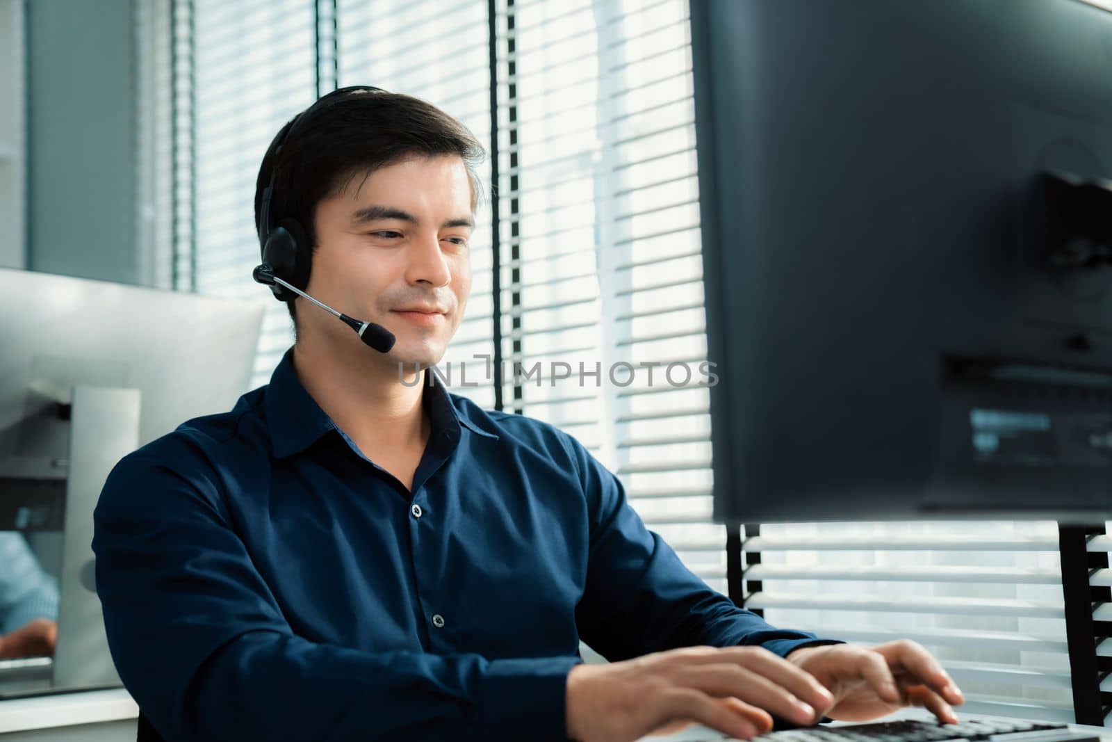 Young competent asian male call center agent working in the office. by biancoblue