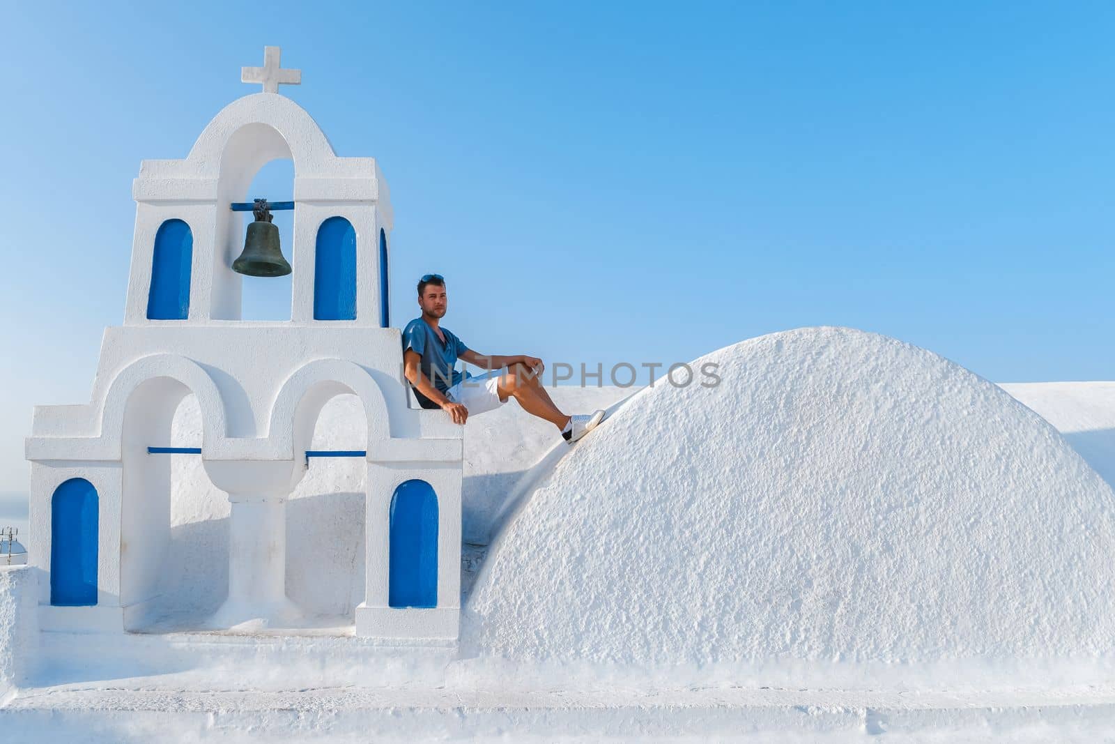 Young men at Oia Santorini Greece on a sunny day during summer with whitewashed homes and churches by fokkebok