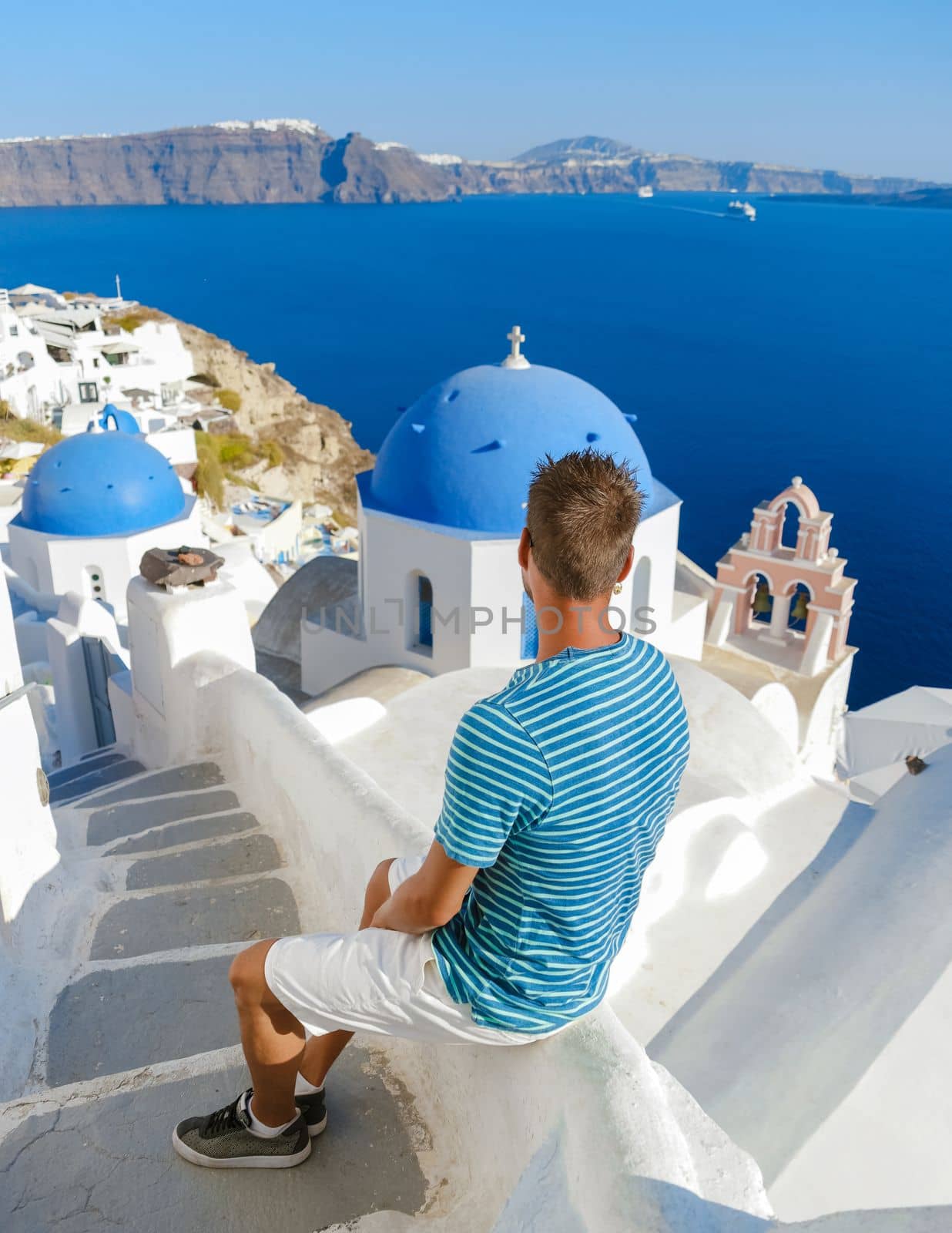 Young men tourists visit Oia Santorini Greece on a sunny day during summer with whitewashed homes and churches, Greek Island Aegean Cyclades