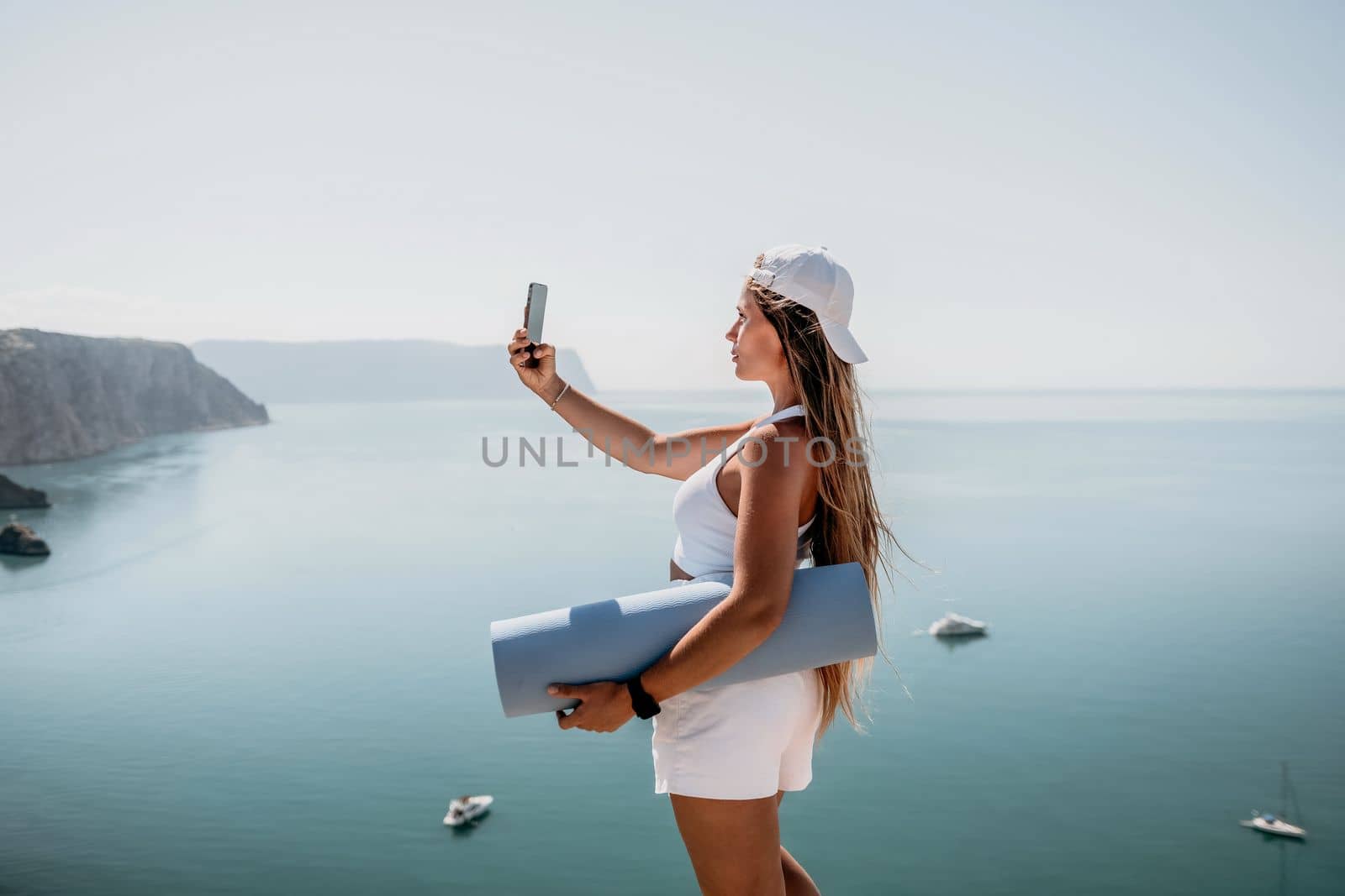 Young woman with black hair, fitness instructor in pink sports leggings and tops, doing pilates on yoga mat with magic pilates ring by the sea on the beach. Female fitness daily yoga concept