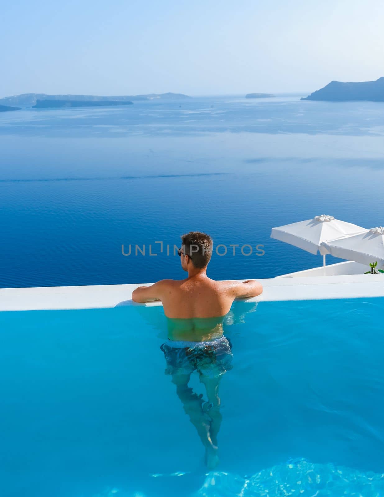 man relaxing in infinity swimming during vacation at Santorini, swimming pool looking out over the Caldera ocean of Santorini, Oia Greece, Greek Island Aegean Cyclades luxury vacation.