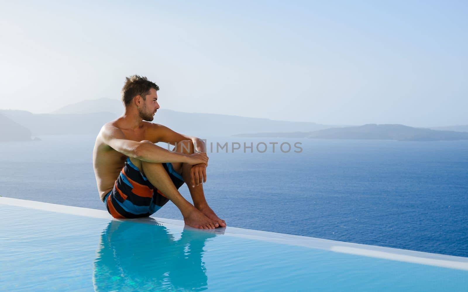 man relaxing in infinity swimming during vacation at Santorini, swimming pool looking out over the Caldera ocean of Santorini, Oia Greece, Greek Island Aegean Cyclades luxury vacation.