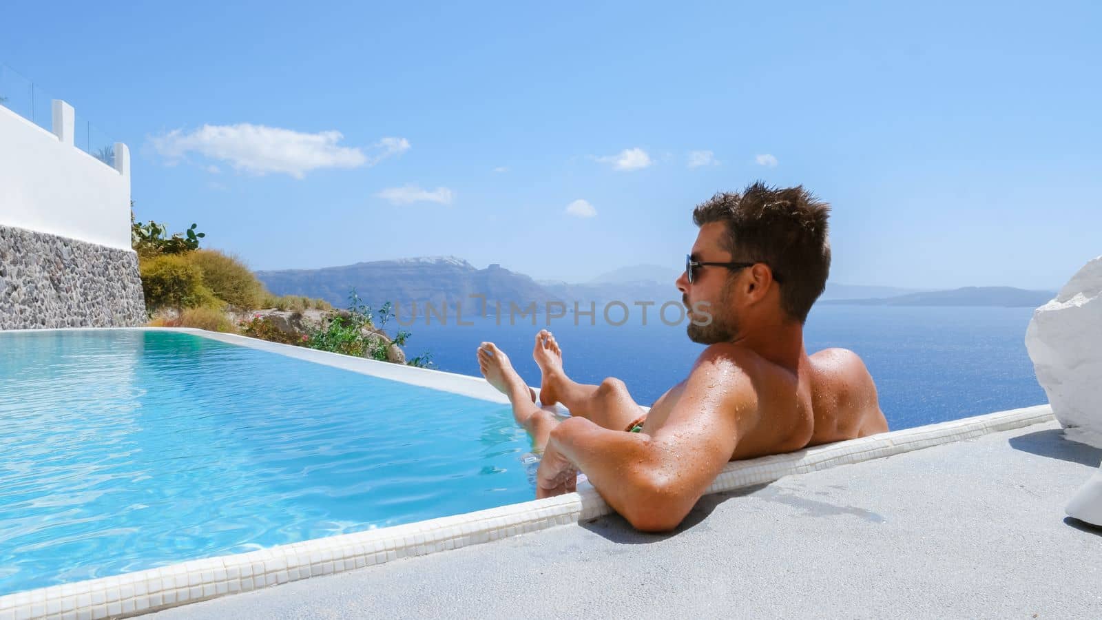 young man relaxing in swimming pool during vacation at Santorini infinity looking out over the ocean by fokkebok