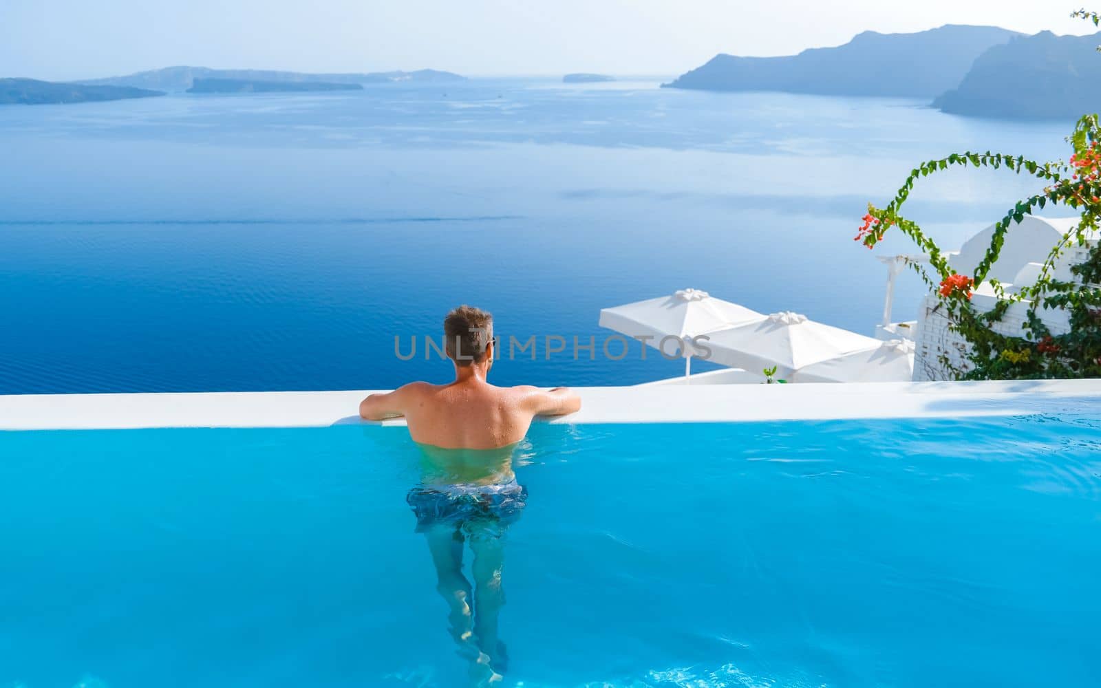 man relaxing in swimming pool during vacation at Santorini infinity looking out over the ocean by fokkebok