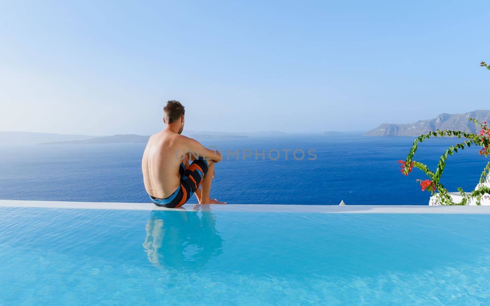 men relaxing in an infinity swimming pool during vacation at Santorini, swimming pool looking out over the Caldera ocean of Santorini, Oia Greece, Greek Island Aegean Cyclades luxury vacation.