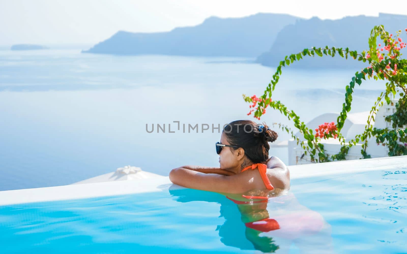 Young Asian women on vacation at Santorini swimming pool looking out over the Caldera ocean of Santorini, Oia Greece, Greek Island Aegean Cyclades.