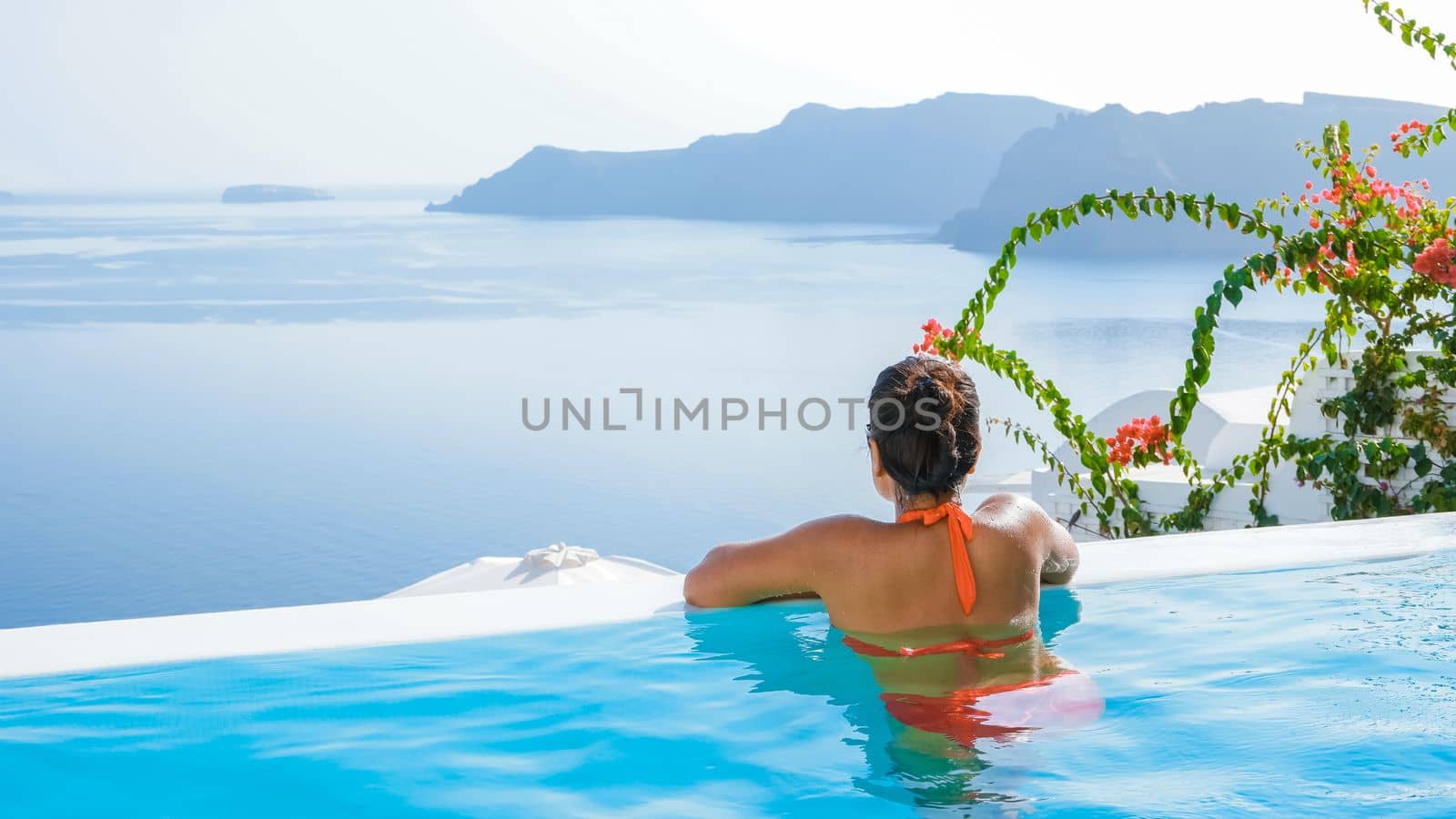 Young Asian women on vacation at Santorini swimming pool looking out over the Caldera ocean of Santorini, Oia Greece, Greek Island Aegean Cyclades.