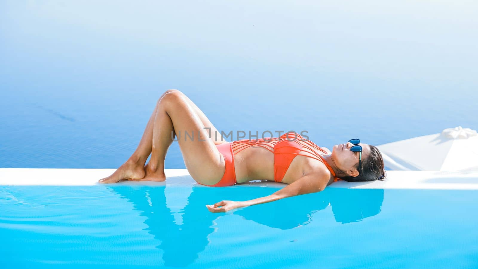 Young Asian women on vacation at Santorini swimming pool looking out over the Caldera ocean of Santorini, Oia Greece, Greek Island Aegean Cyclades.