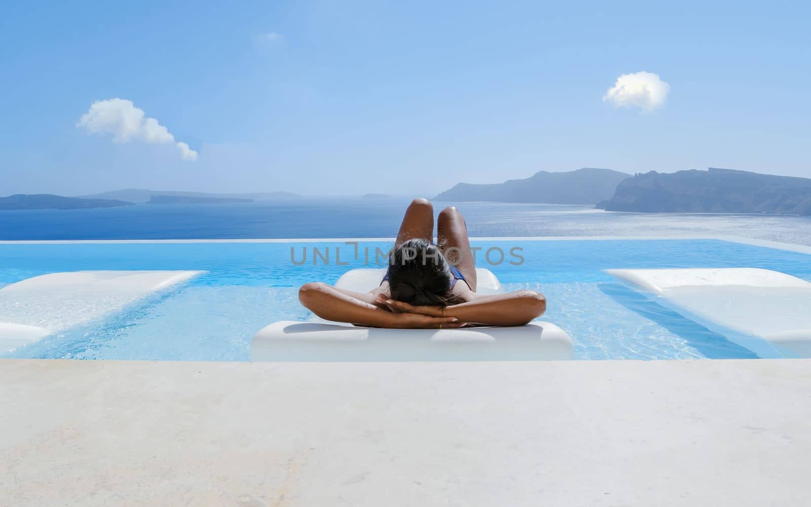 Young Asian women on vacation at Santorini swimming pool looking out over the Caldera ocean of Santorini, Oia Greece, Greek Island Aegean Cyclades.