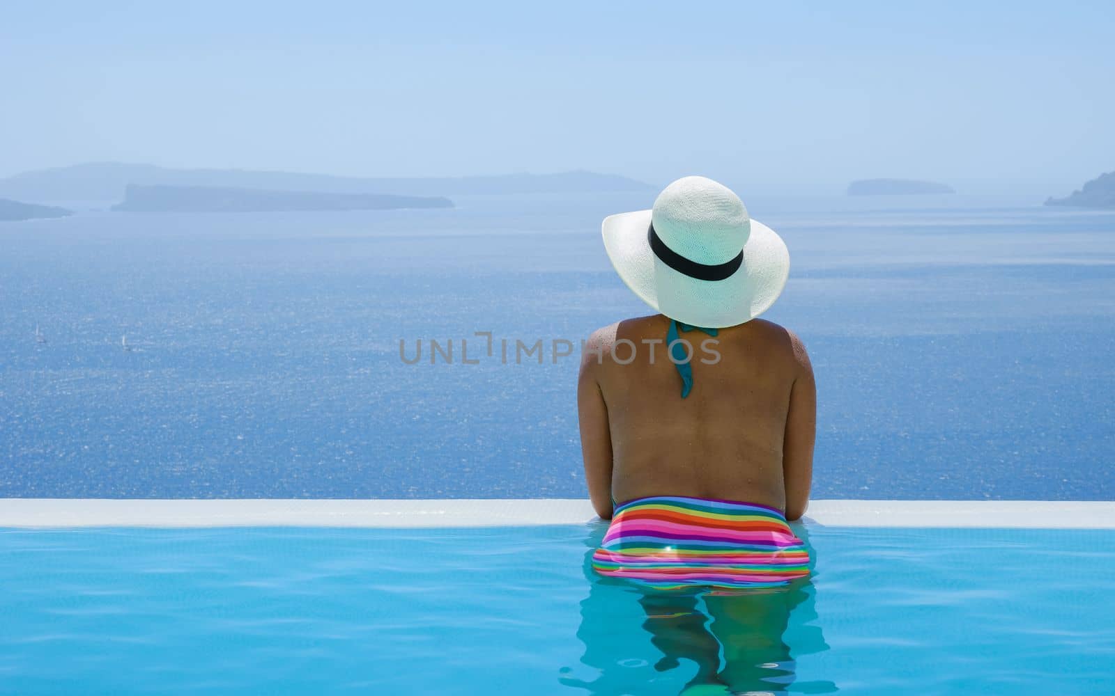 Young Asian women on vacation at Santorini swimming pool looking out over the Caldera ocean of Santorini, Oia Greece, Greek Island Aegean Cyclades.