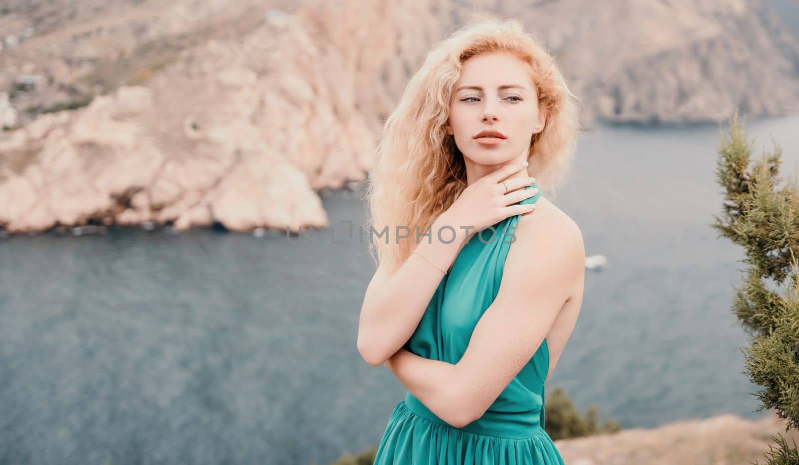 Side view a Young beautiful sensual woman in a mint long dress posing on a volcanic rock high above the sea during sunset. Girl on the nature on overcast sky background. Fashion photo
