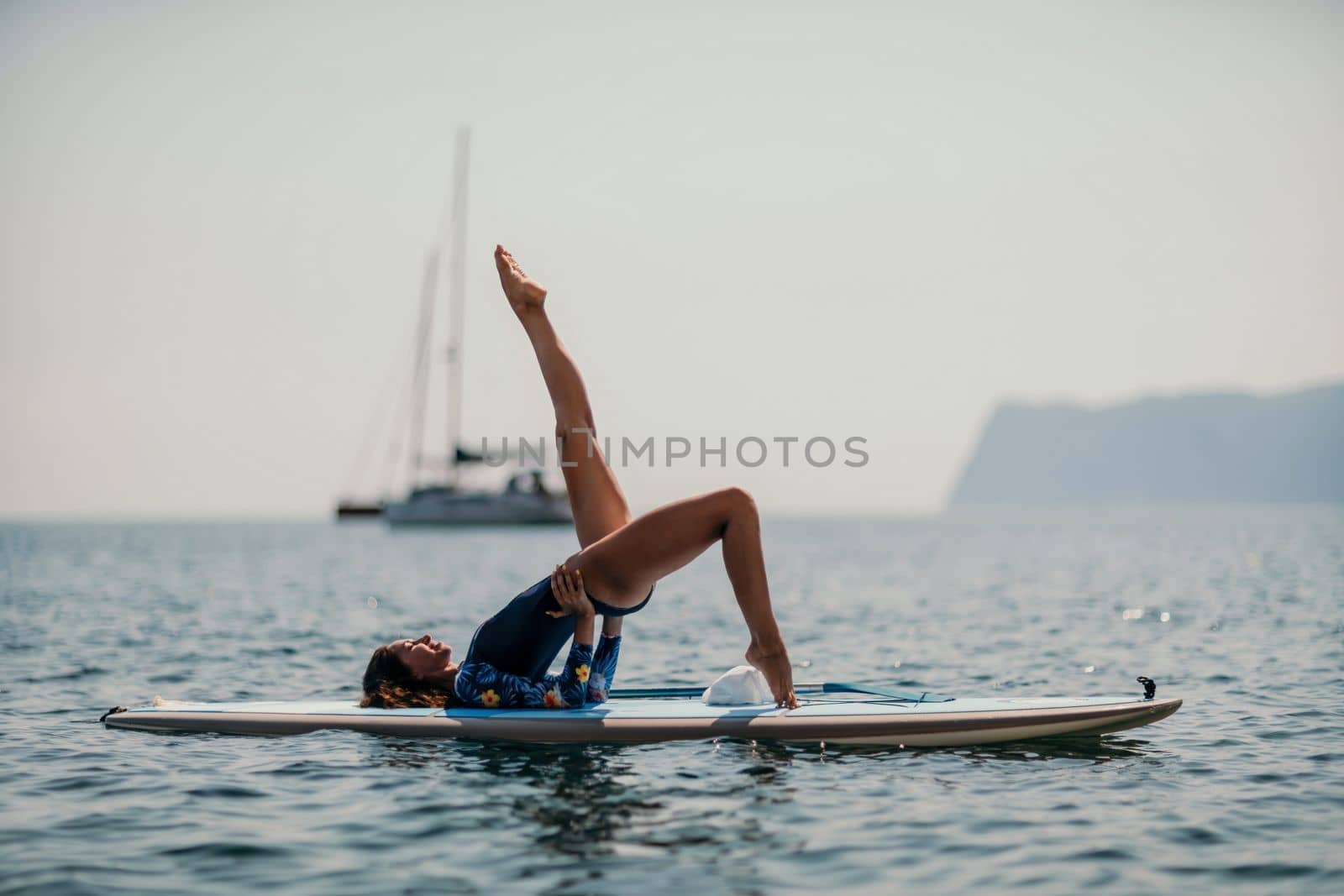 Woman sup yoga. Middle age sporty woman practising yoga pilates on paddle sup surfboard. Female stretching doing workout on sea water. Modern individual hipster outdoor summer sport activity