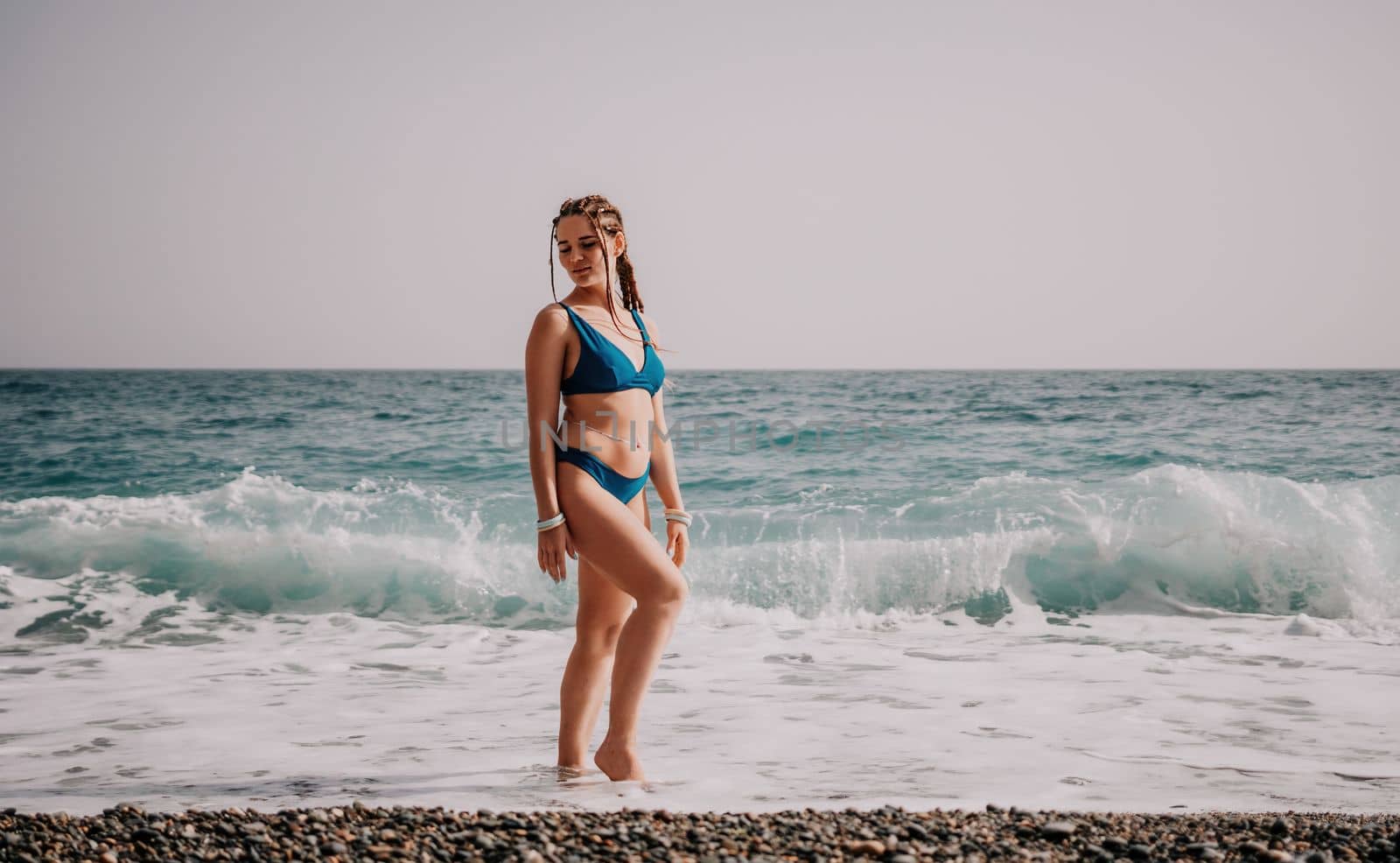 Beach vacation. Hot beautiful woman in sunhat and bikini standing with her arms raised to her head enjoying looking view of beach ocean on hot summer day.