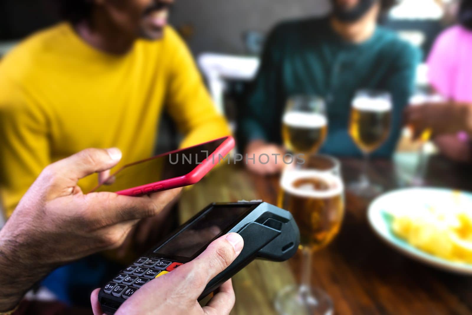 Close up of man hand paying bill with mobile phone at a bar. Selective focus on foreground. Copy space. Lifestyle concept.