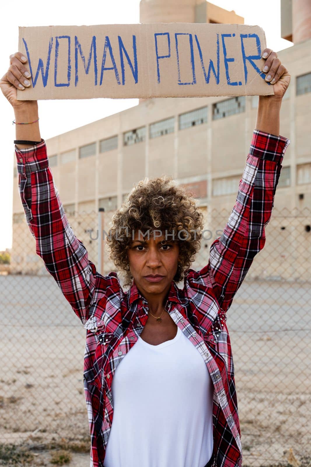 Confident African american demonstration protester looking at camera holding a woman power sign above her head. by Hoverstock