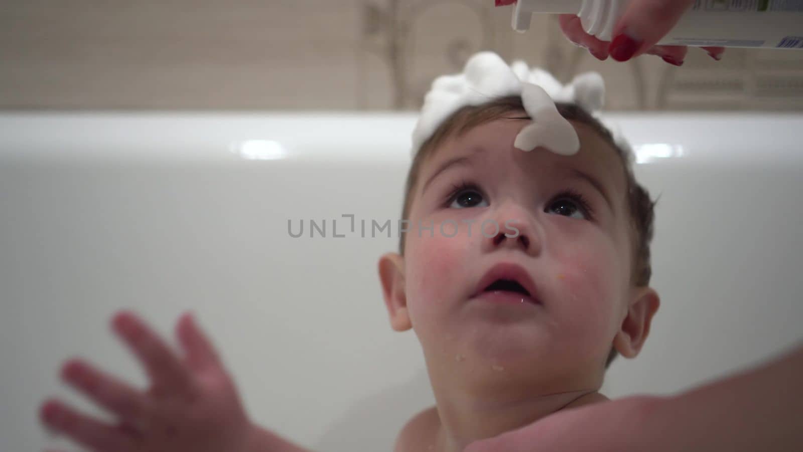 The little son bathes in the bath. Shampoo foam is applied to the child's head. Boy close-up. 4k