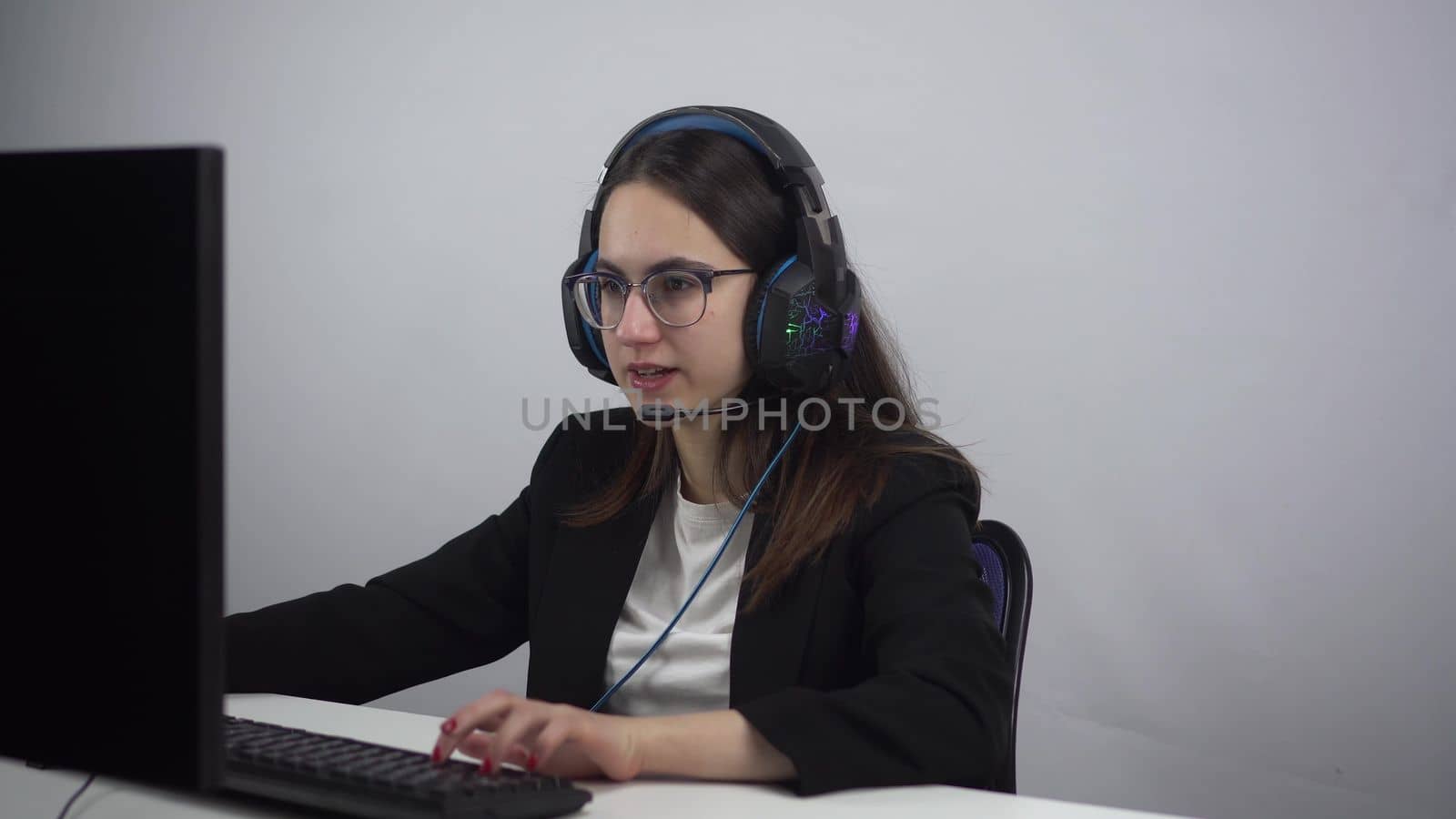 Businesswoman sits at her workplace and plays a computer game. Young woman in a jacket and glasses with headphones. 4k