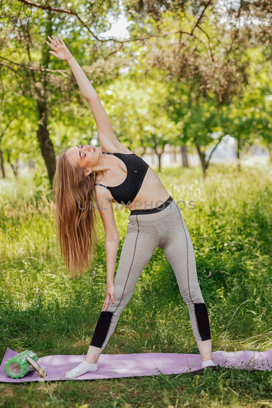 Overweight young woman is training on sports ground. An obese female does slopes outdoors. Doing sports in quarantine. Side view portrait of black lady during workout on fresh air at summer day.