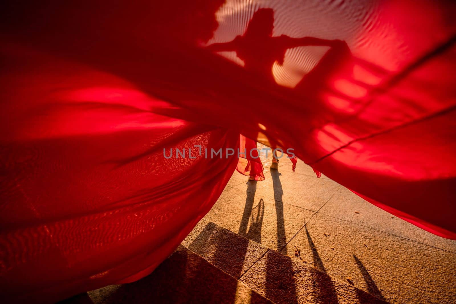 Sunrise red dress. A woman in a long red dress against the backdrop of sunrise, bright golden light of the sun's rays. The concept of femininity, harmony