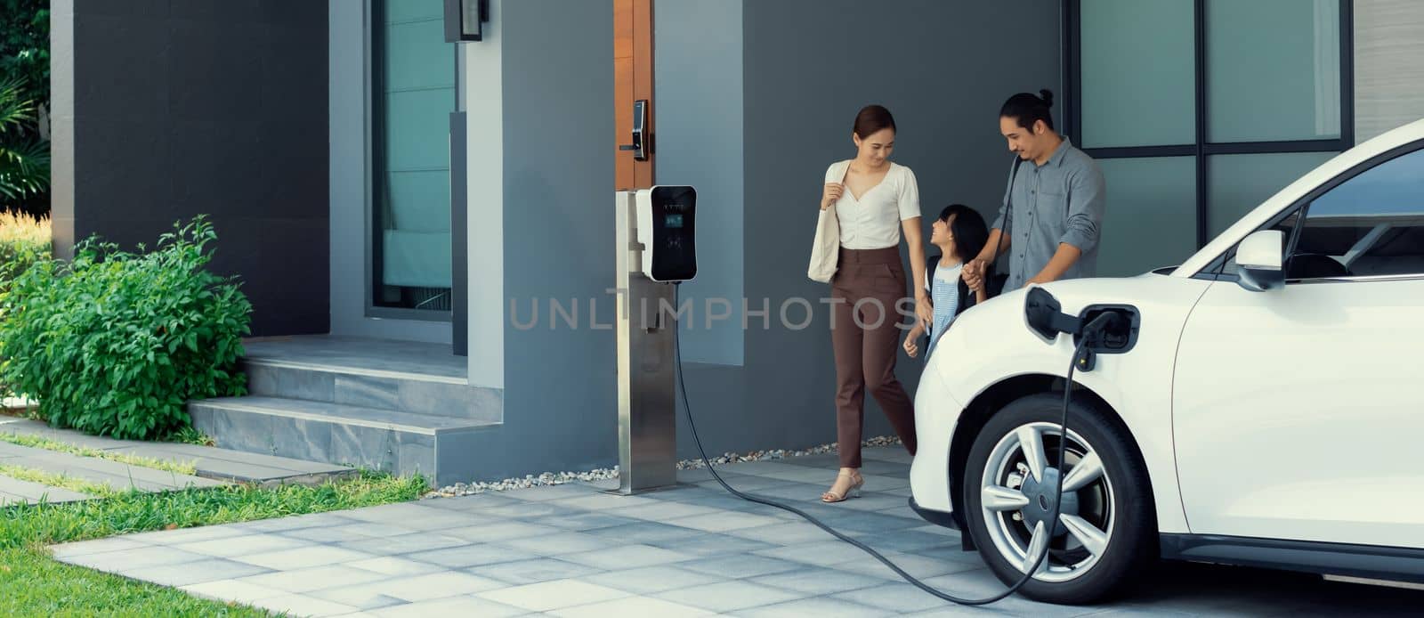 Progressive young parents and daughter living in a home with an electric car. by biancoblue