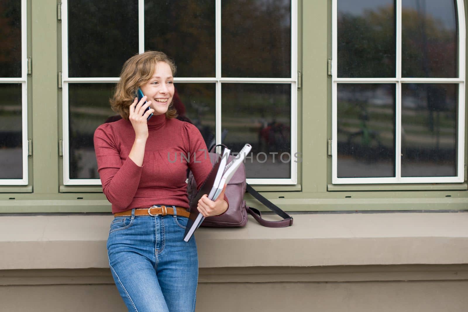 a young caucasian girl returns to college, stands with a backpack and notebooks and talks on the phone in a laugh, back to school, High quality photo