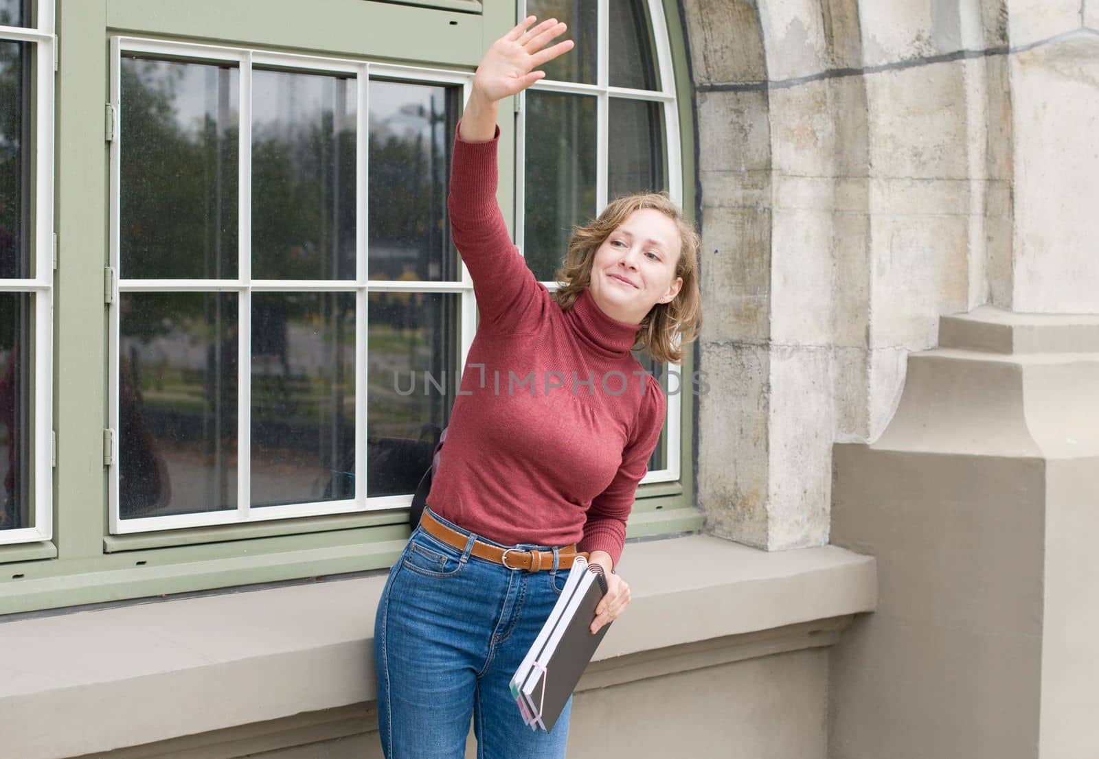 young caucasian girl going back to school, standing with a notebooks and waving to someone in the distance, High quality photo