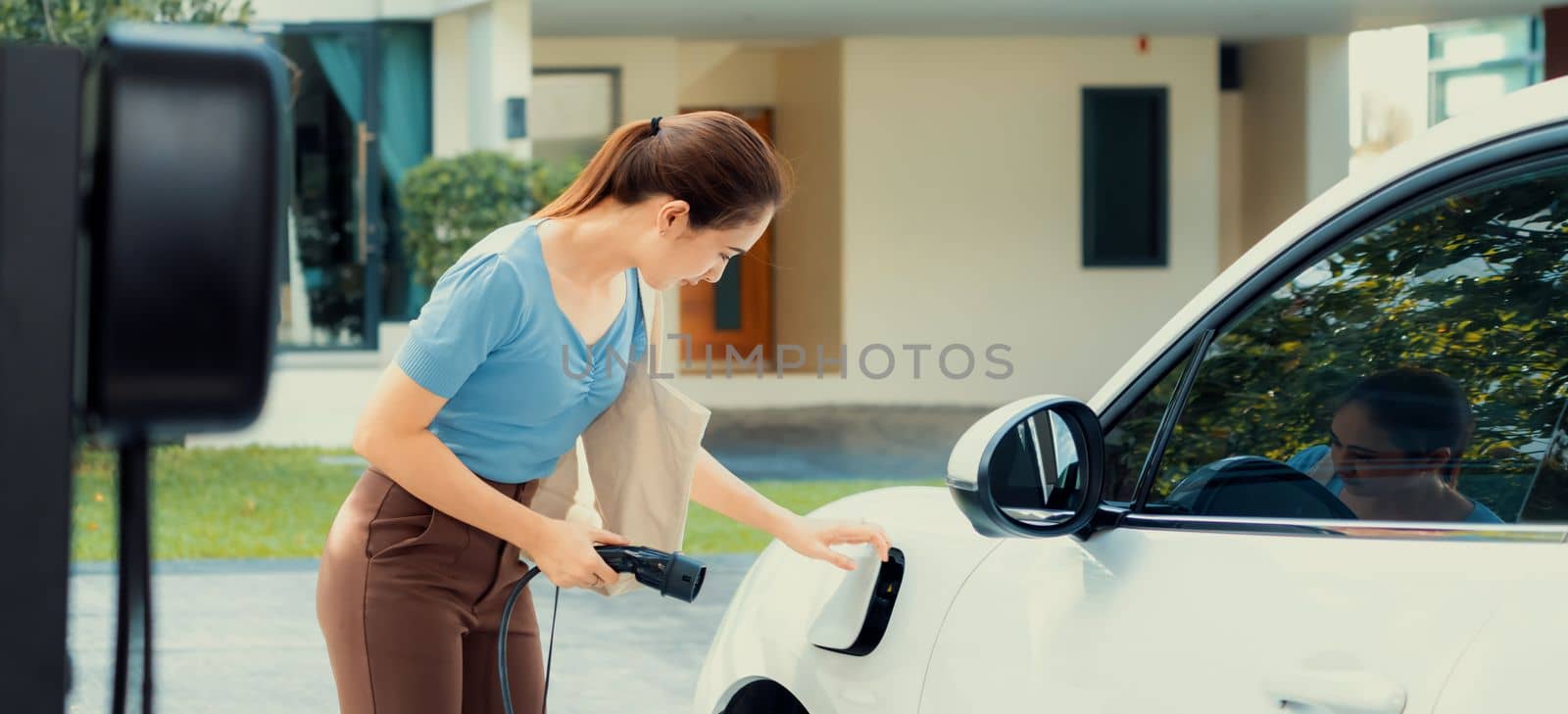 Progressive woman recharge her EV car at home charging station. by biancoblue