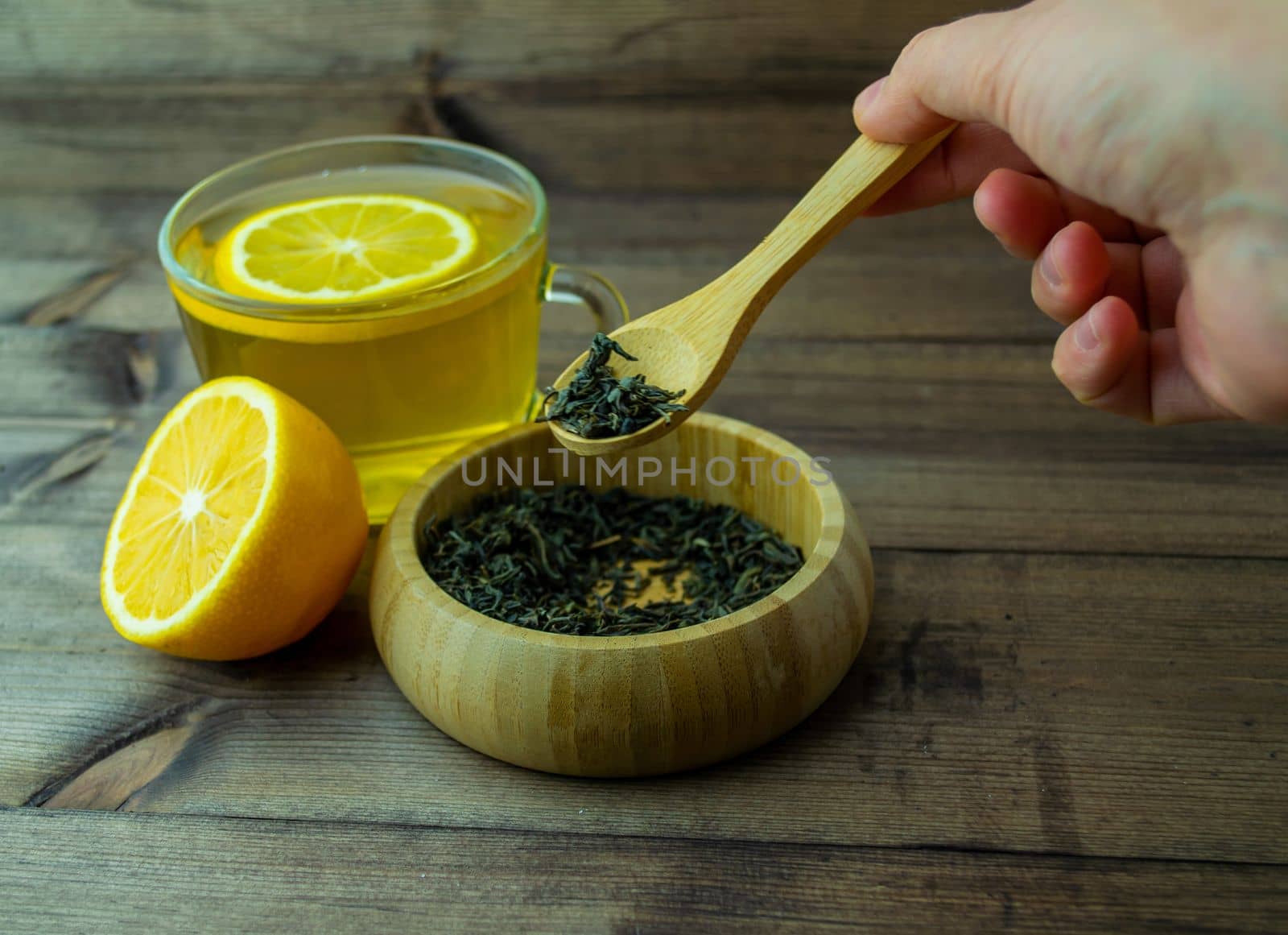 Green tea in a mug, lemon and dry tea. The female hand of a man takes dry tea with a spoon.
