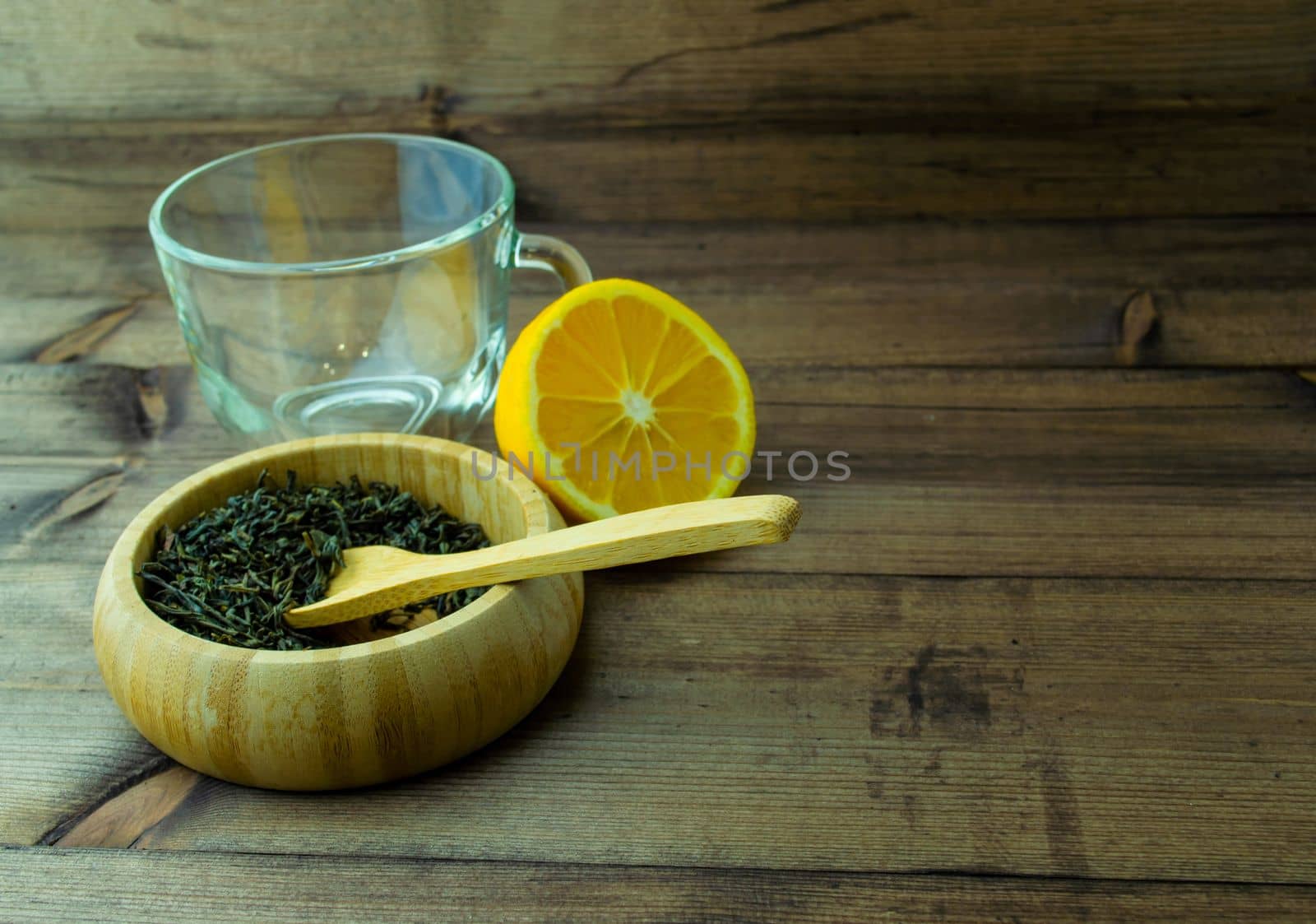 Glass mug with dried green tea and cut lemon. Glass mug with dried green tea and lemon on a wooden table.