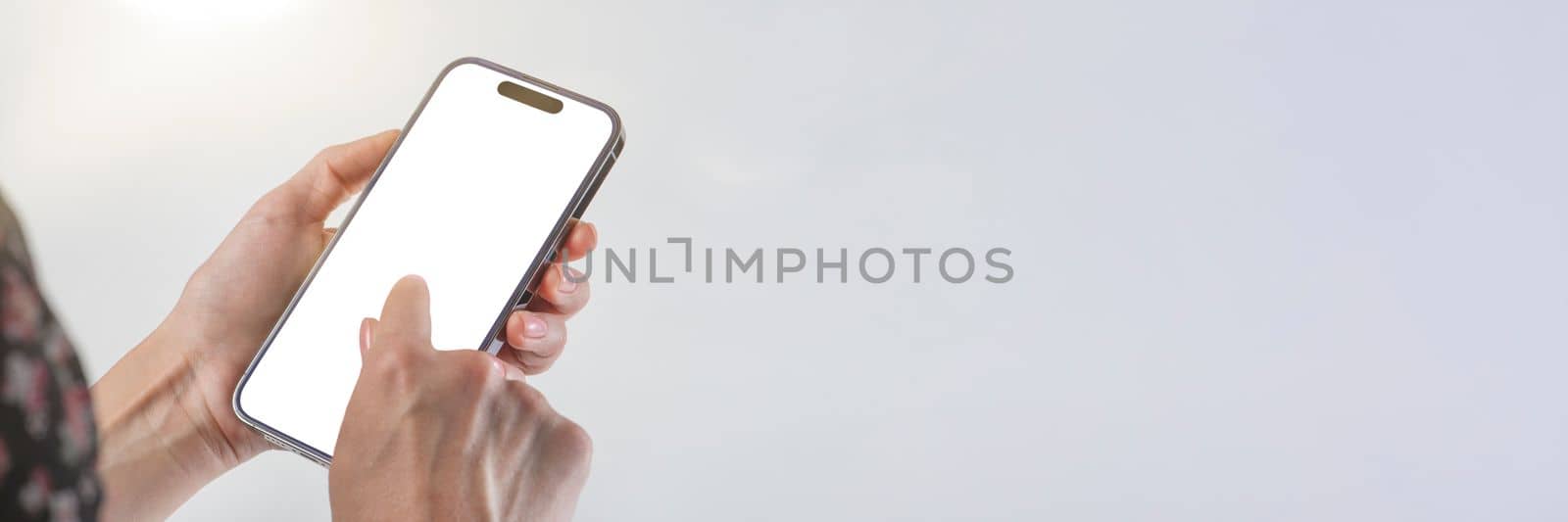 Phone in hand on a white background. A woman holds a phone in her hand on a white background and presses with her finger on a blank white screen. Finger tap on phone screen with copy space