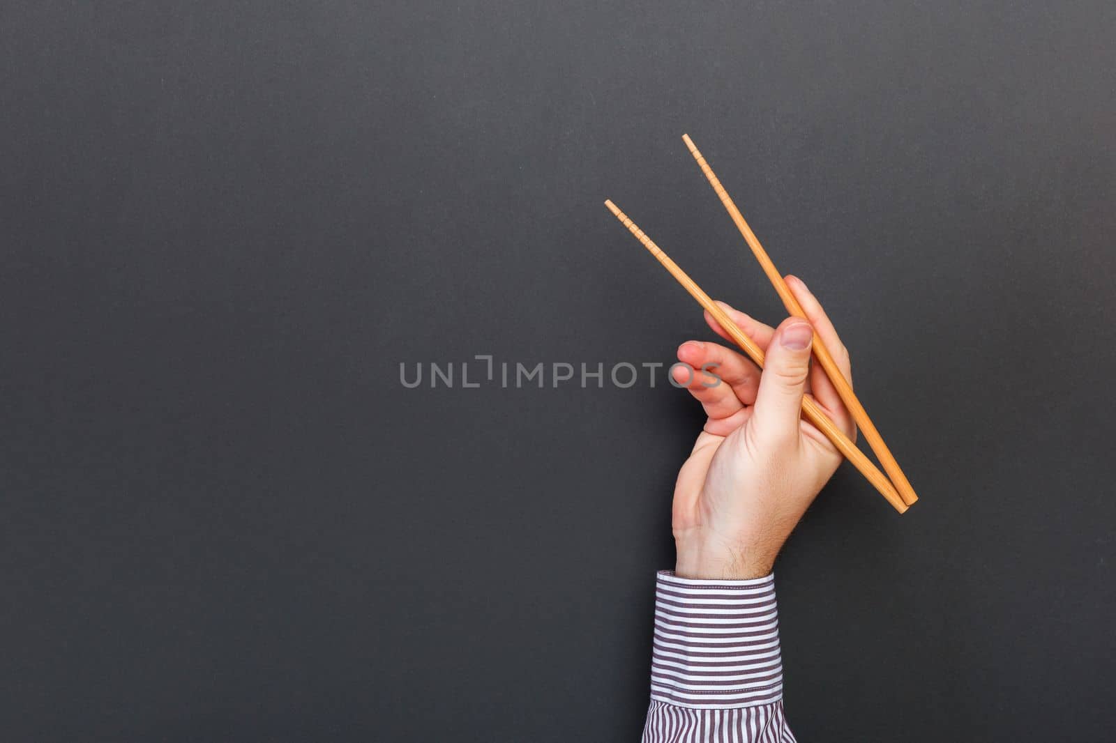 Creative image of wooden chopsticks in male hands on black background. Japanese and chinese food with copy space.