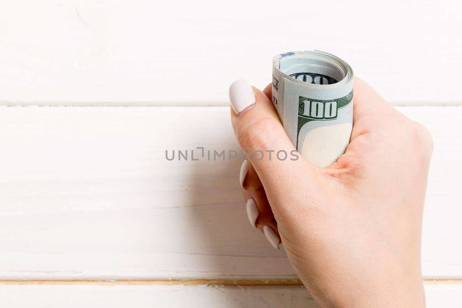 Female hand holding tightly a bundle of money. Top view of one hundred dollars on wooden background. Investment concept.