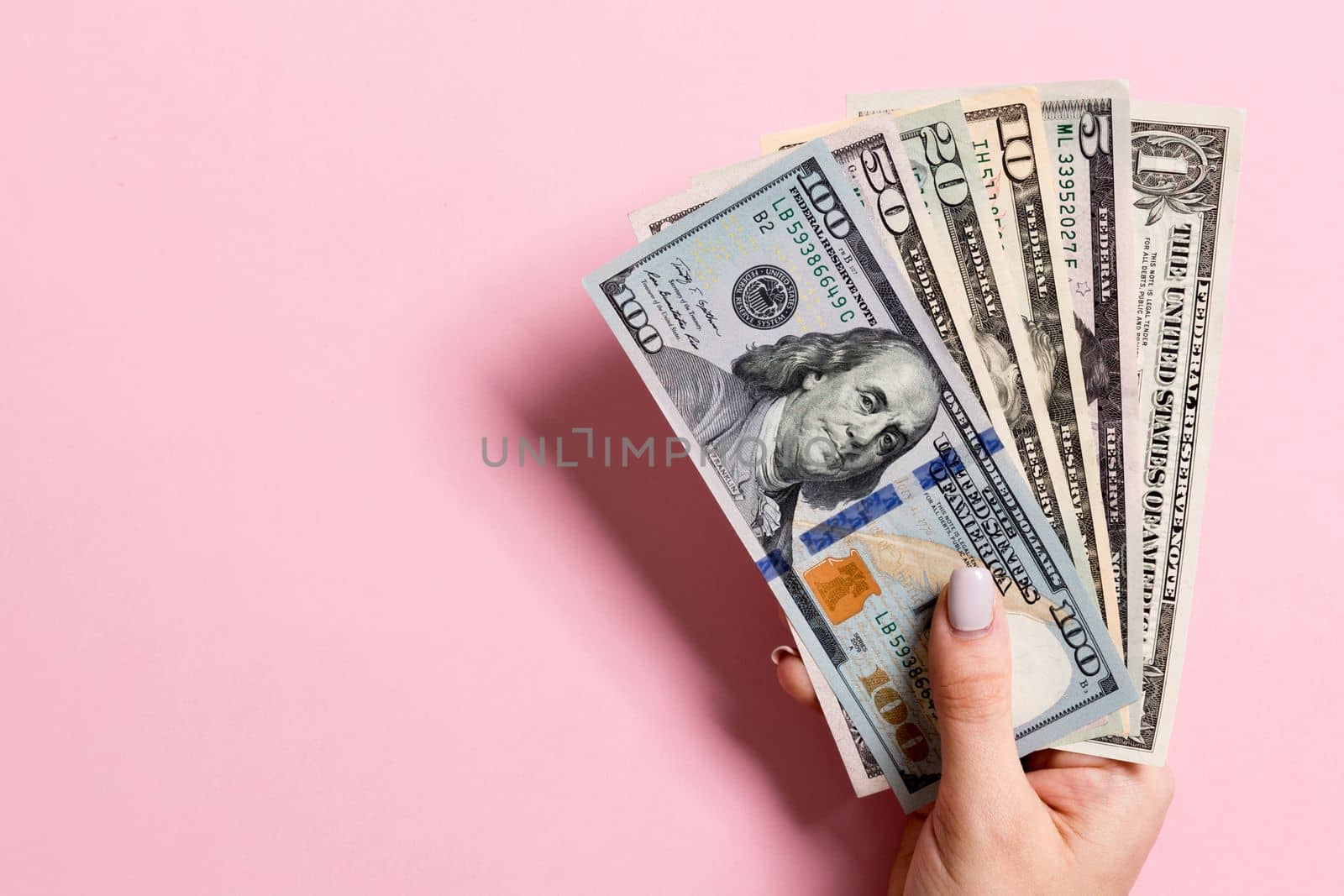 Top view of female hand holding a fan of money on colorful background. Various dollar bills. Credit and debt concept with copy space.