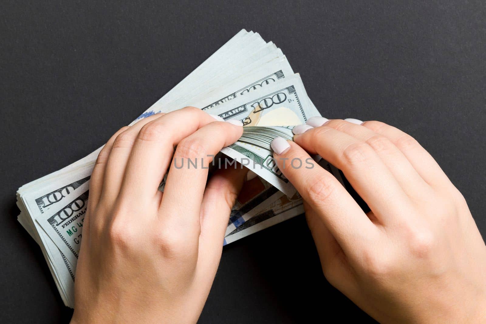 Top view of a businesswoman's hands counting one hundred dollar banknotes on colorful background. Success and wealth concept.