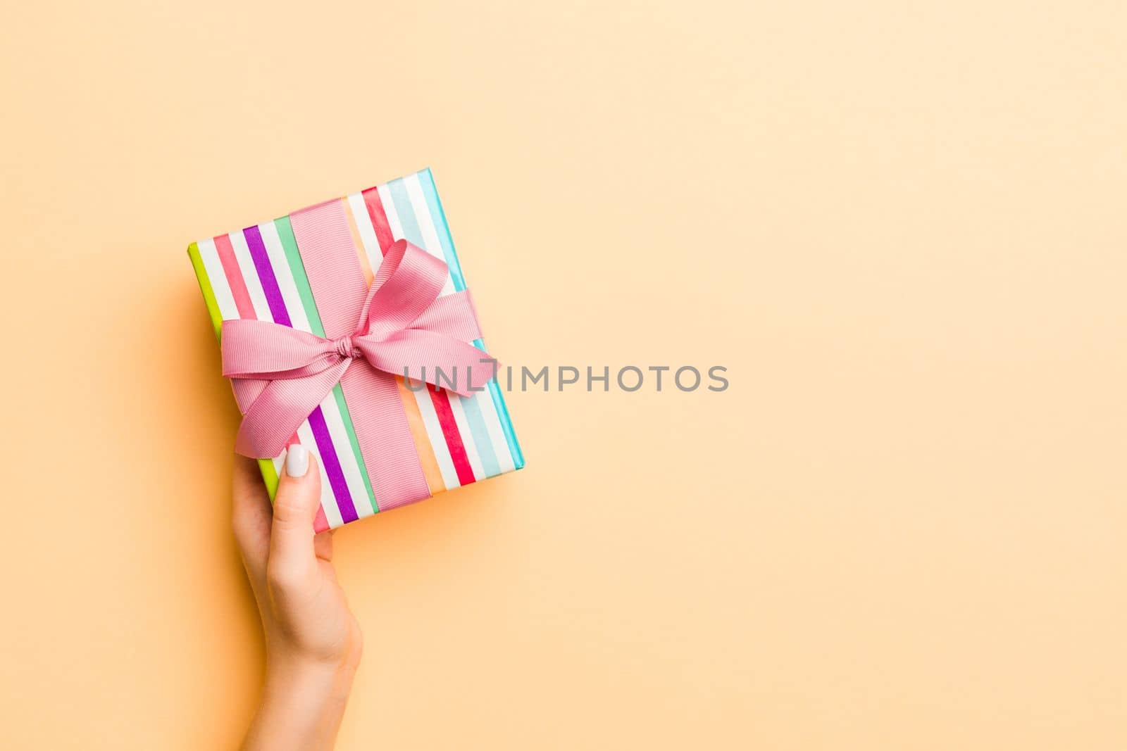 Flat lay of woman hands holding gift wrapped and decorated with bow on gold background with copy space. Christmas and holiday concept.