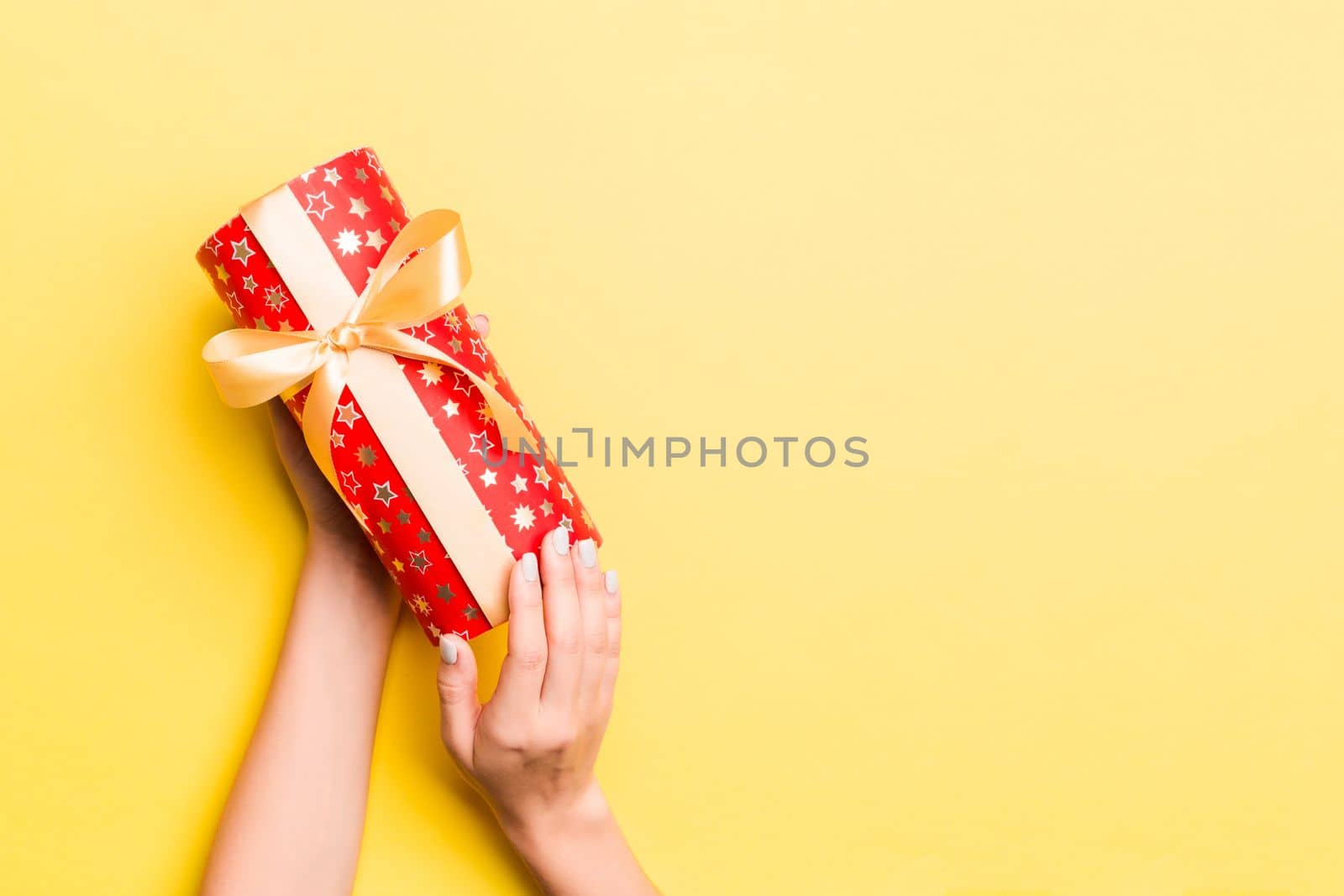 Woman arms holding gift box with colored ribbon on yellow table background, top view and copy space for you design.