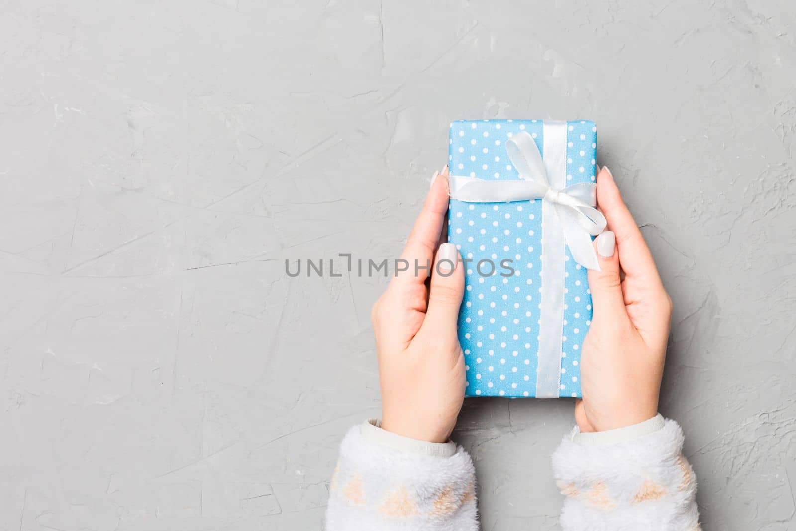 Female hands holding present on grey cement background. Festive backdrop for Christmas holidays or other holiday . Flat lay style top view with copy space.