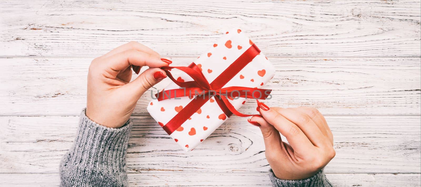 Woman hands give wrapped valentine or other holiday handmade present in paper with red ribbon. Present box, red heart of gift on table, Top view banner with copy space for you design Toned web banner.