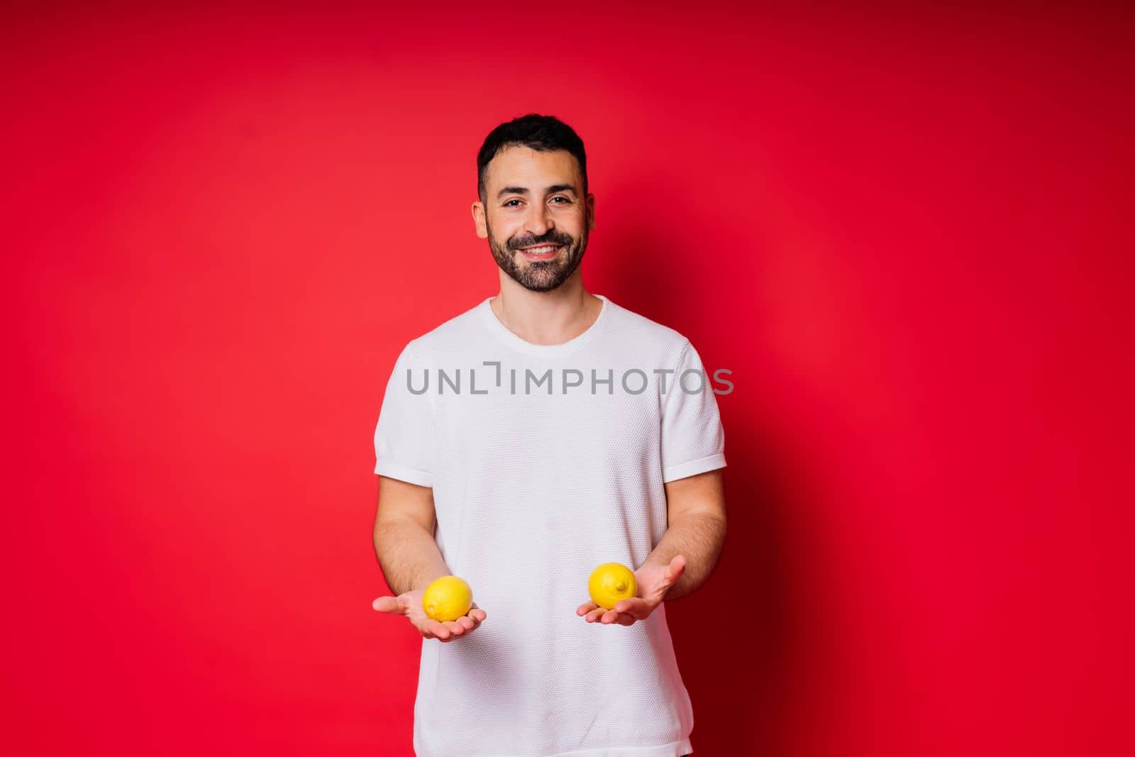 Portrait of young bearded man holding lemons in both hands on an isolated red background