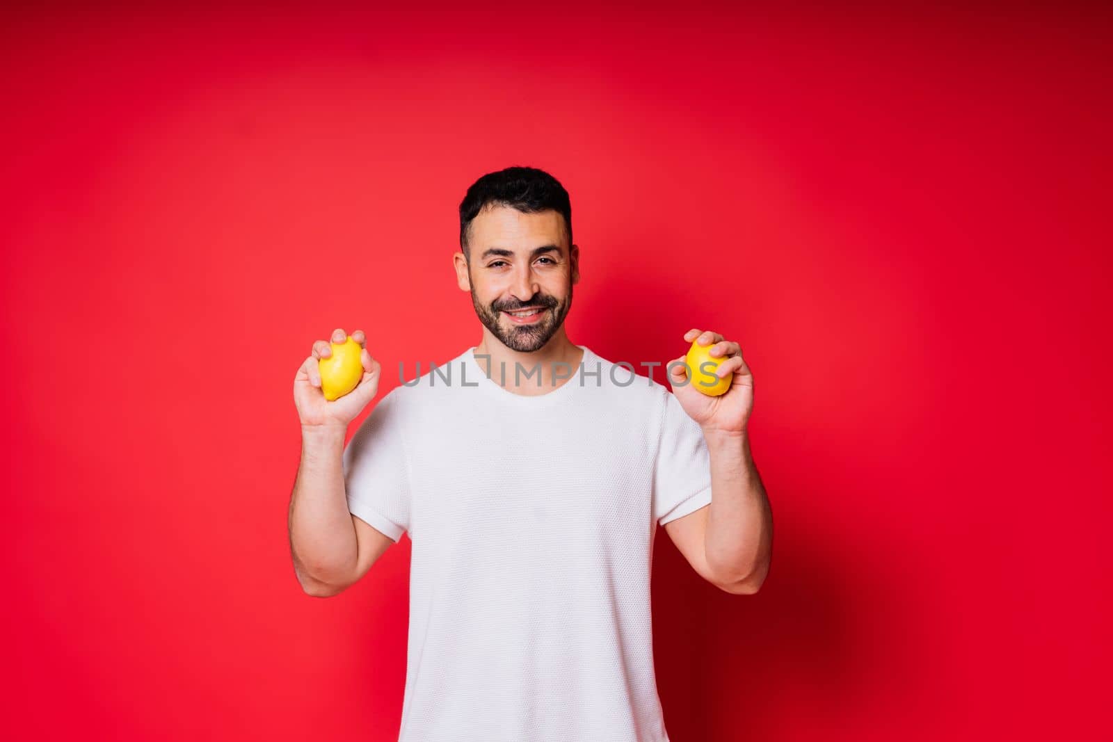 Portrait of young bearded man holding lemons in both hands on an isolated red background