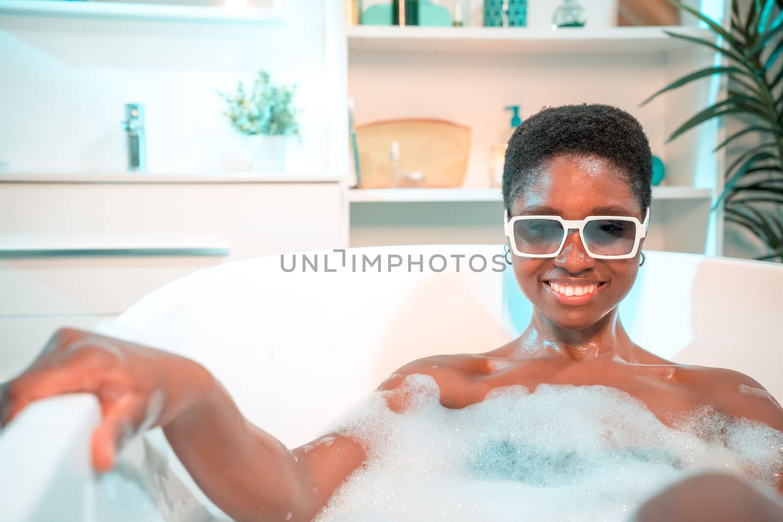 Portrait of an attractive African woman in foam bathtub with sunglasses looking at camera smiling. by PaulCarr