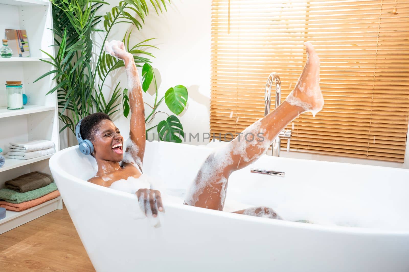 Excited woman wearing headphones happy dancing in foam bath in a sunny morning routine. Happiness. by PaulCarr